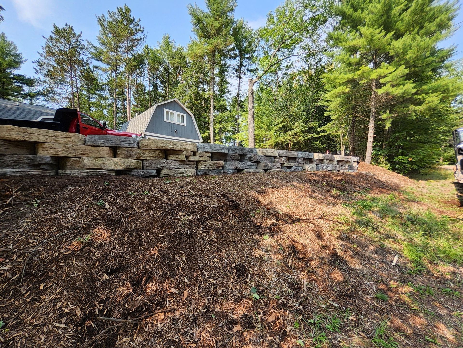 A small barn is sitting on top of a hill next to a stone wall.