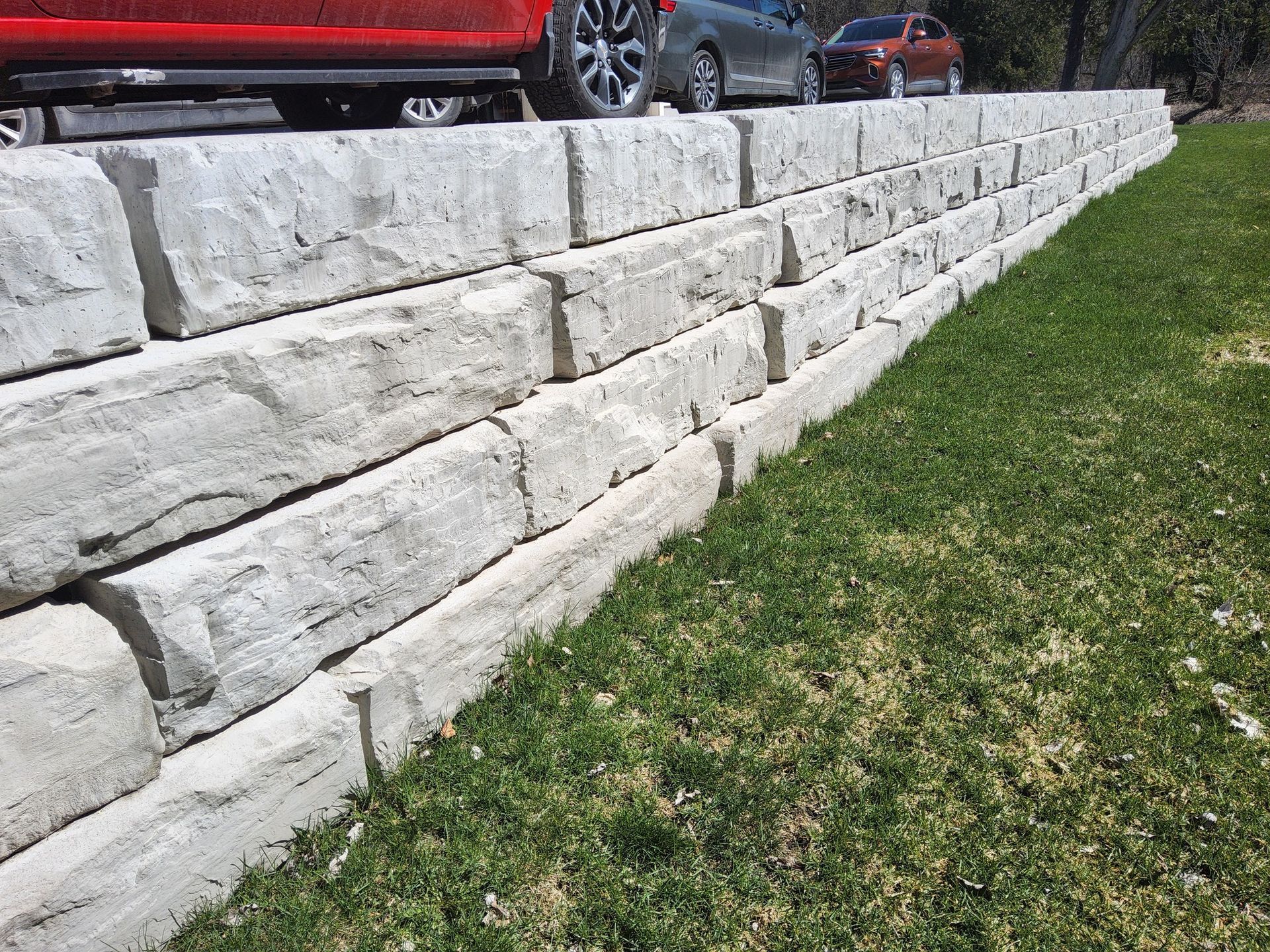 A red car is parked next to a stone wall.