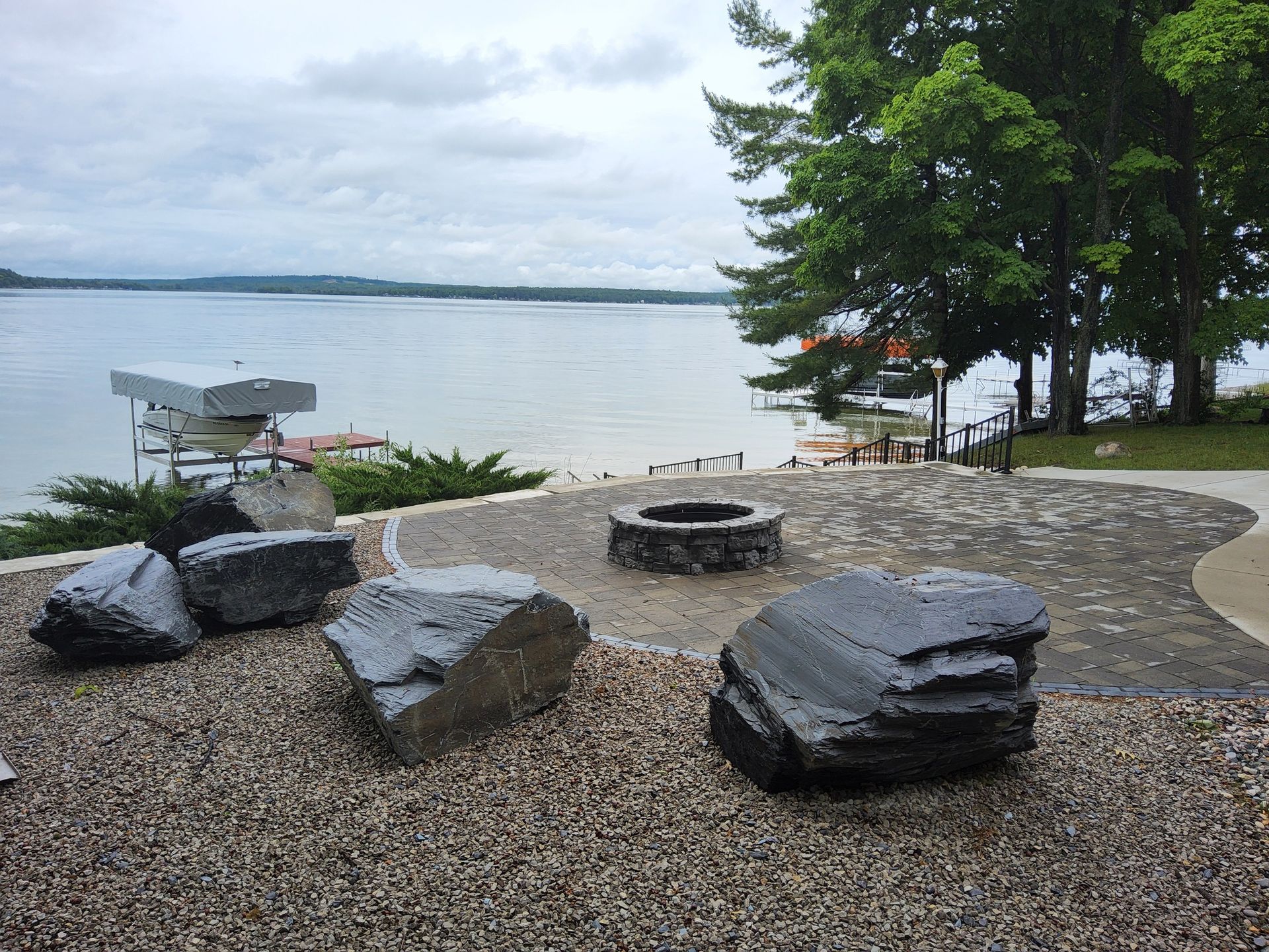 A fire pit in the middle of a gravel area next to a lake.