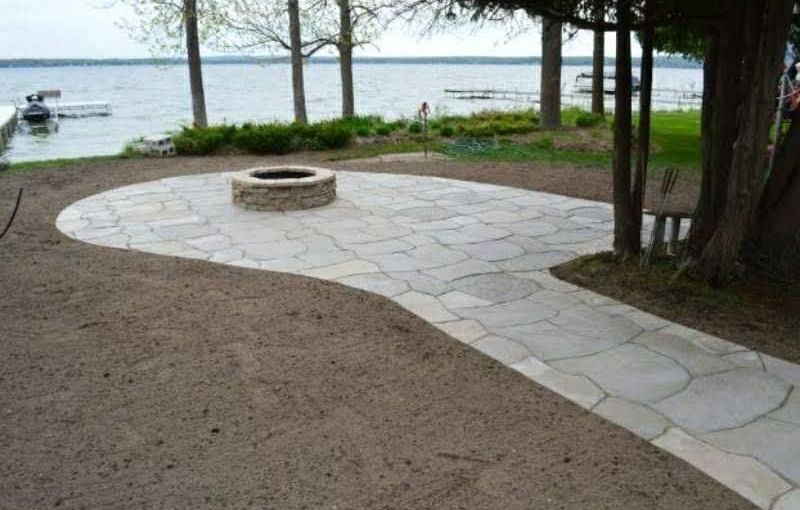 A fire pit is in the middle of a patio next to a lake.