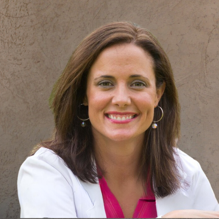 A woman wearing a white jacket and a pink shirt smiles for the camera