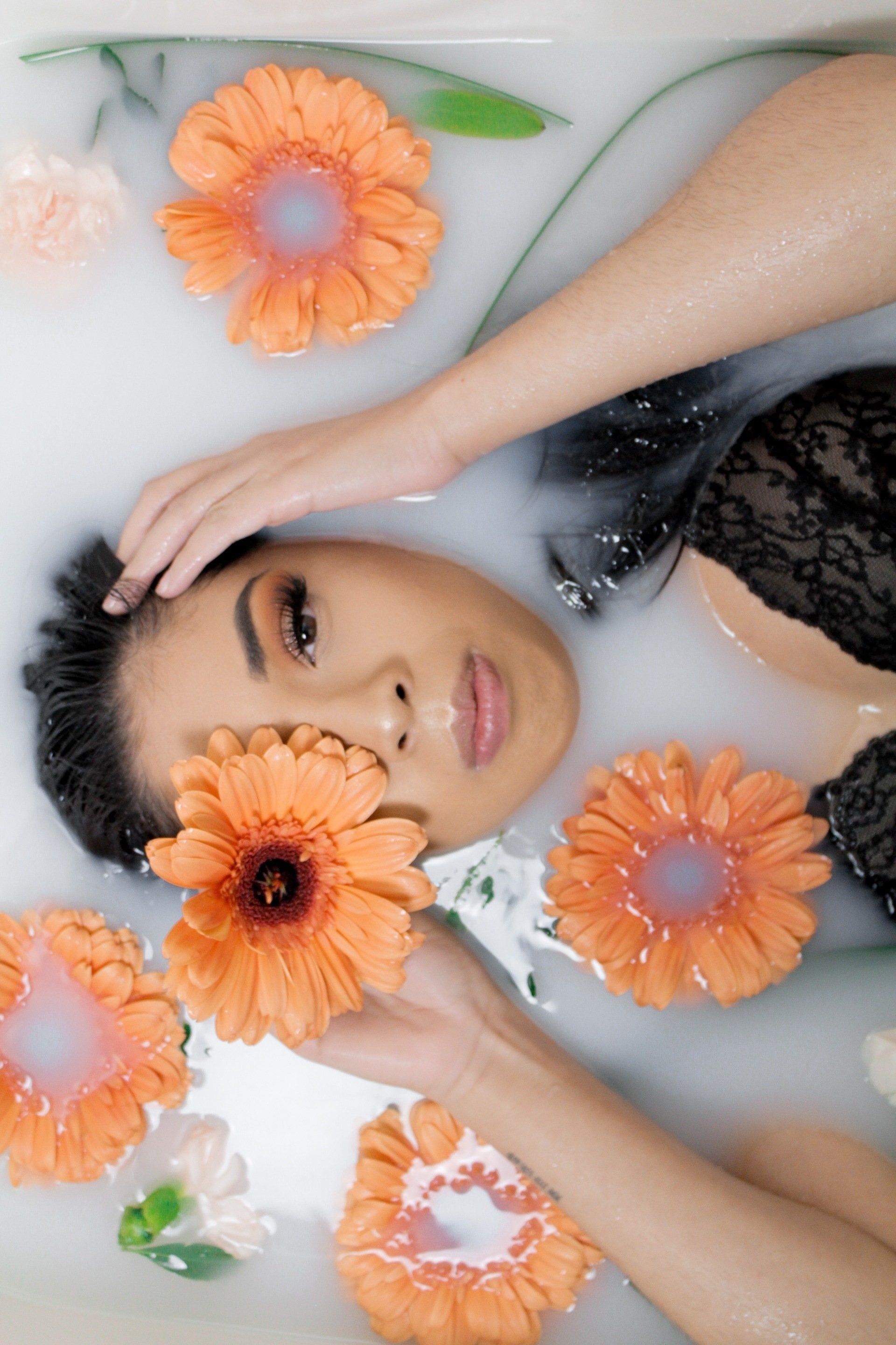 A woman is laying in a bathtub filled with milk and flowers.