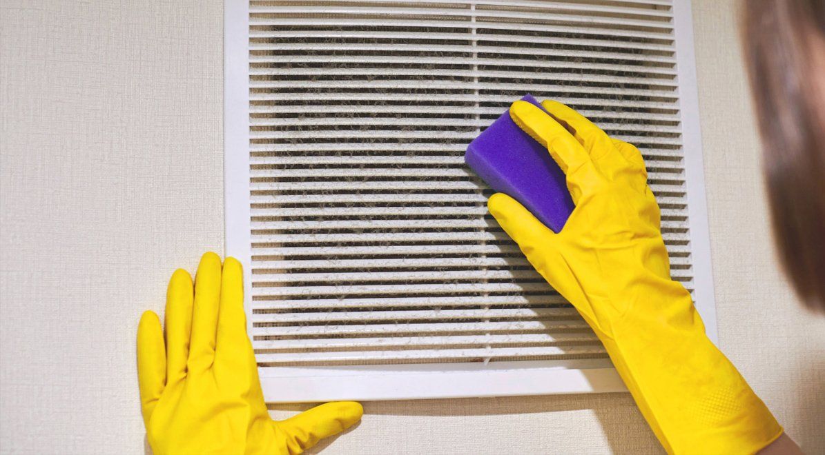 A homeowner wearing yellow rubber gloves using a sponge to wipe air vent