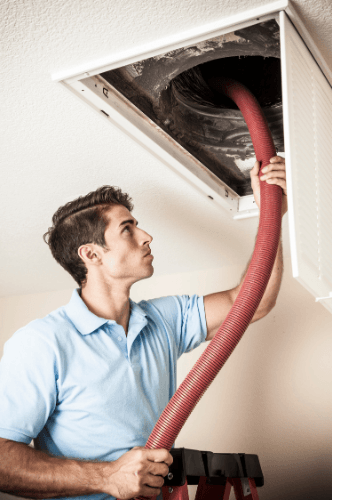 A man is cleaning an air vent with a red hose.