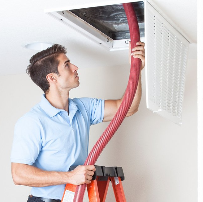 Technician standing on a ladder and feeding a hose into ceiling air duct