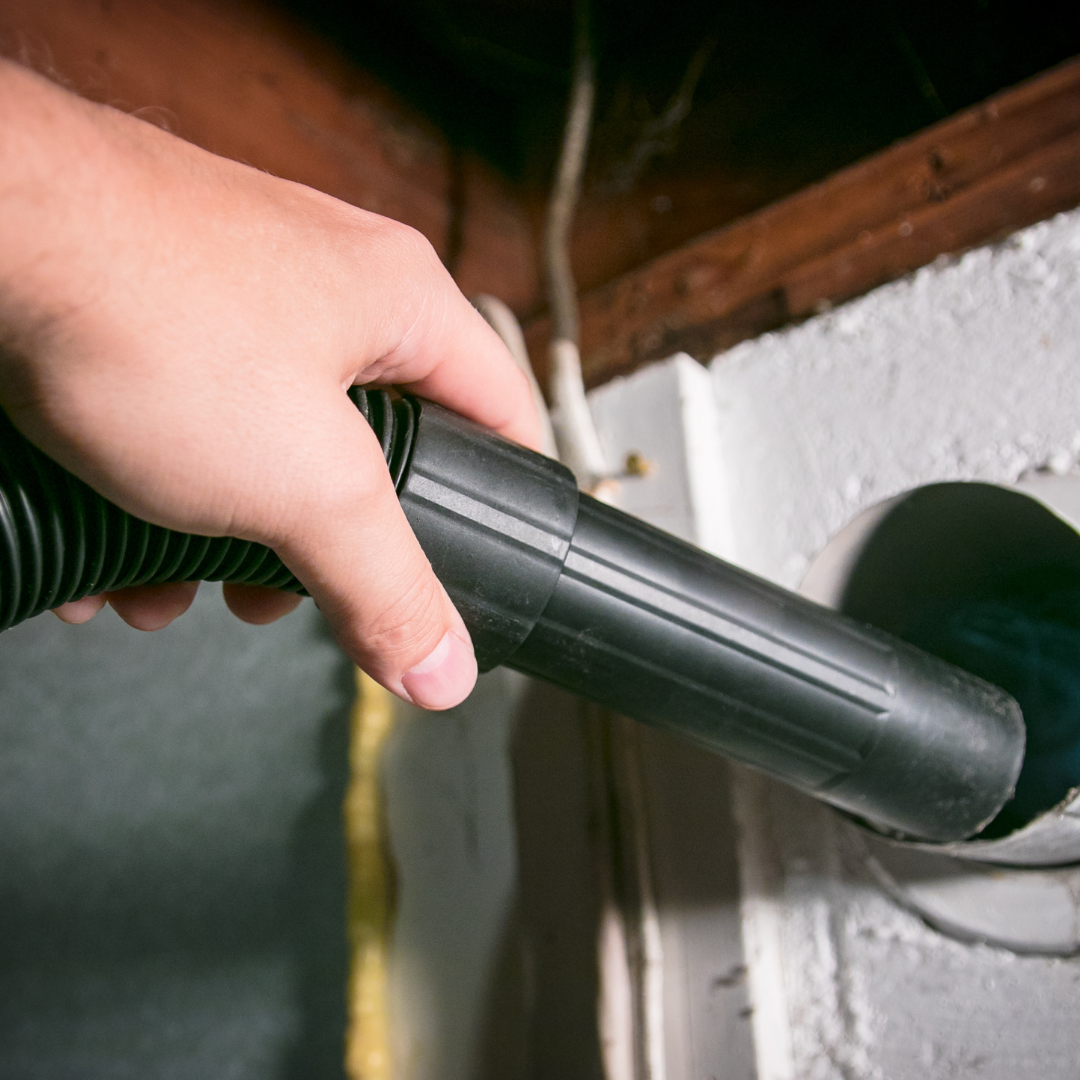 A person is using a vacuum cleaner to clean a dryer vent