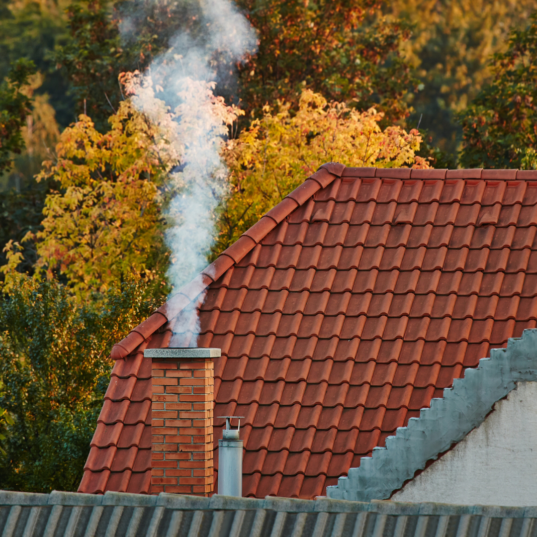 A column of smoke rising out of the chimney atop a tiled roof