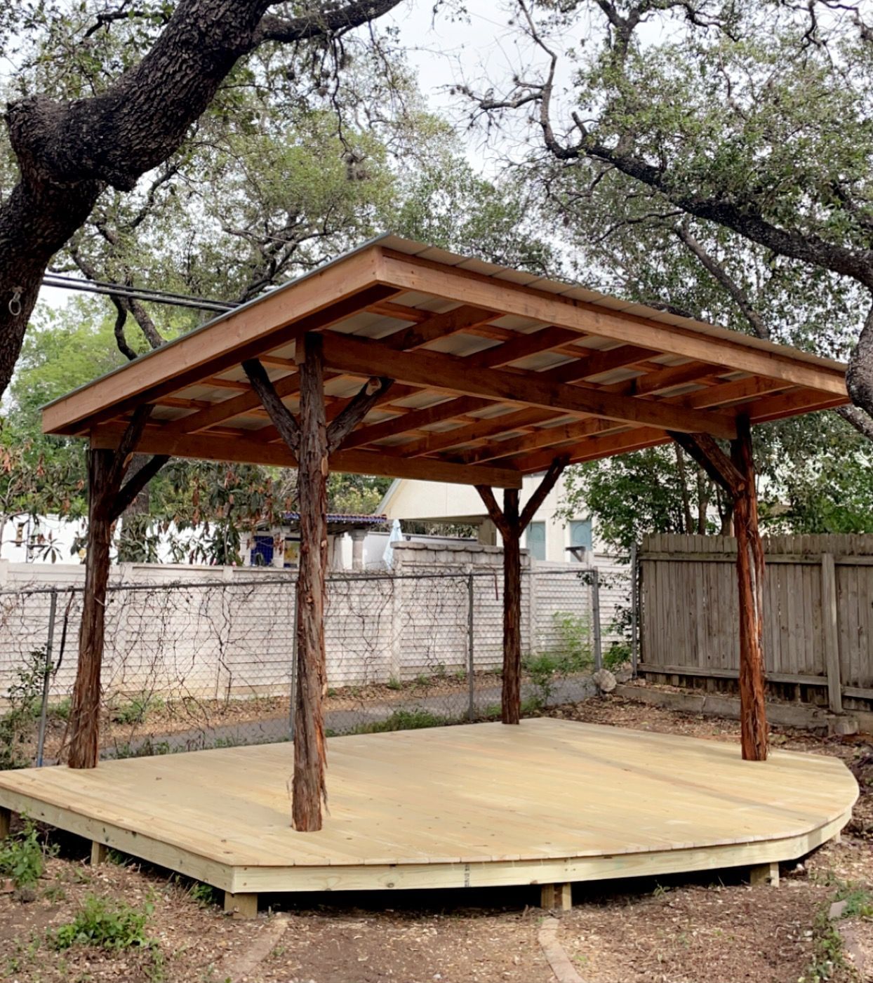 A wooden gazebo with a roof is sitting in the middle of a yard.