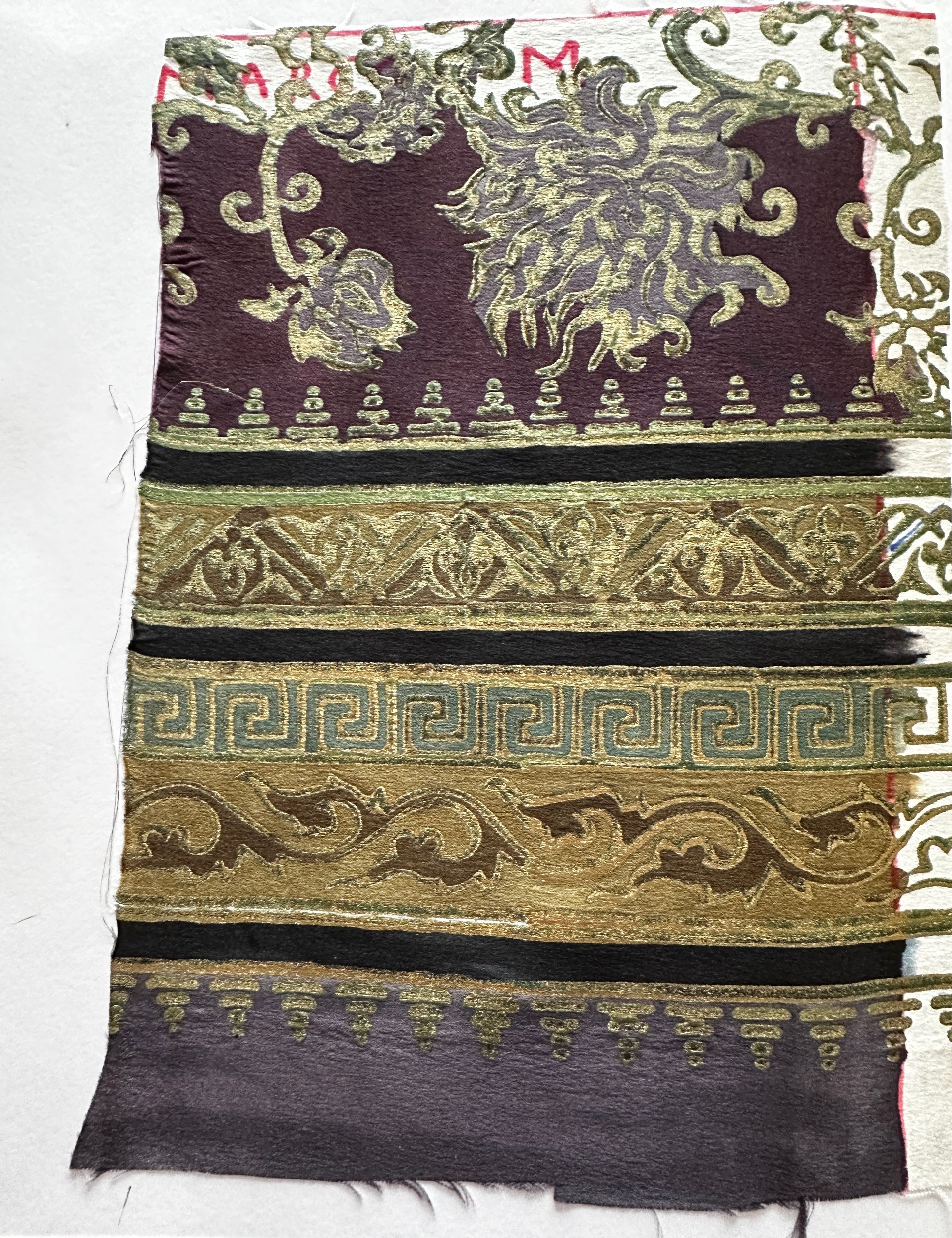 Fabric swatch with dark purple top, gold floral designs, and decorative bands in gold and black.