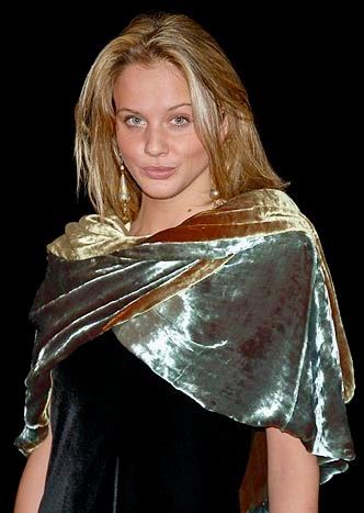 Blonde person wearing a gold velvet shawl over a black dress, looking at the viewer.