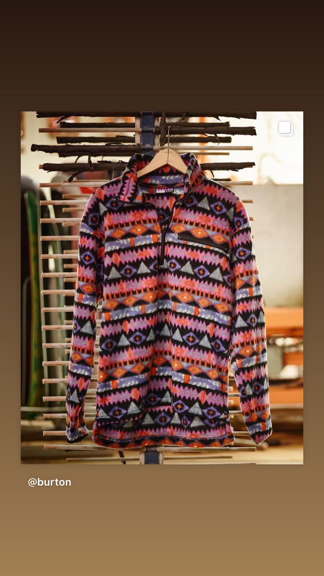 A patterned long-sleeved shirt hangs on a wooden hanger against a blurred background.