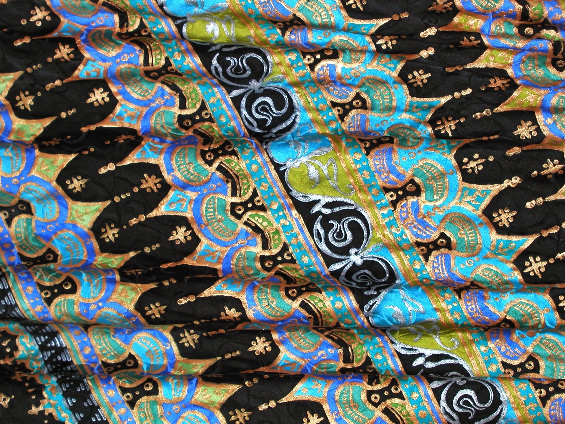 Colorful batik textile with repeating patterns of black, blue, and green.