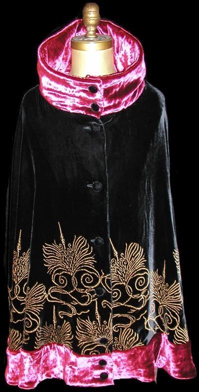 Black velvet cape with gold embroidery, bright pink collar and hem, on a mannequin.