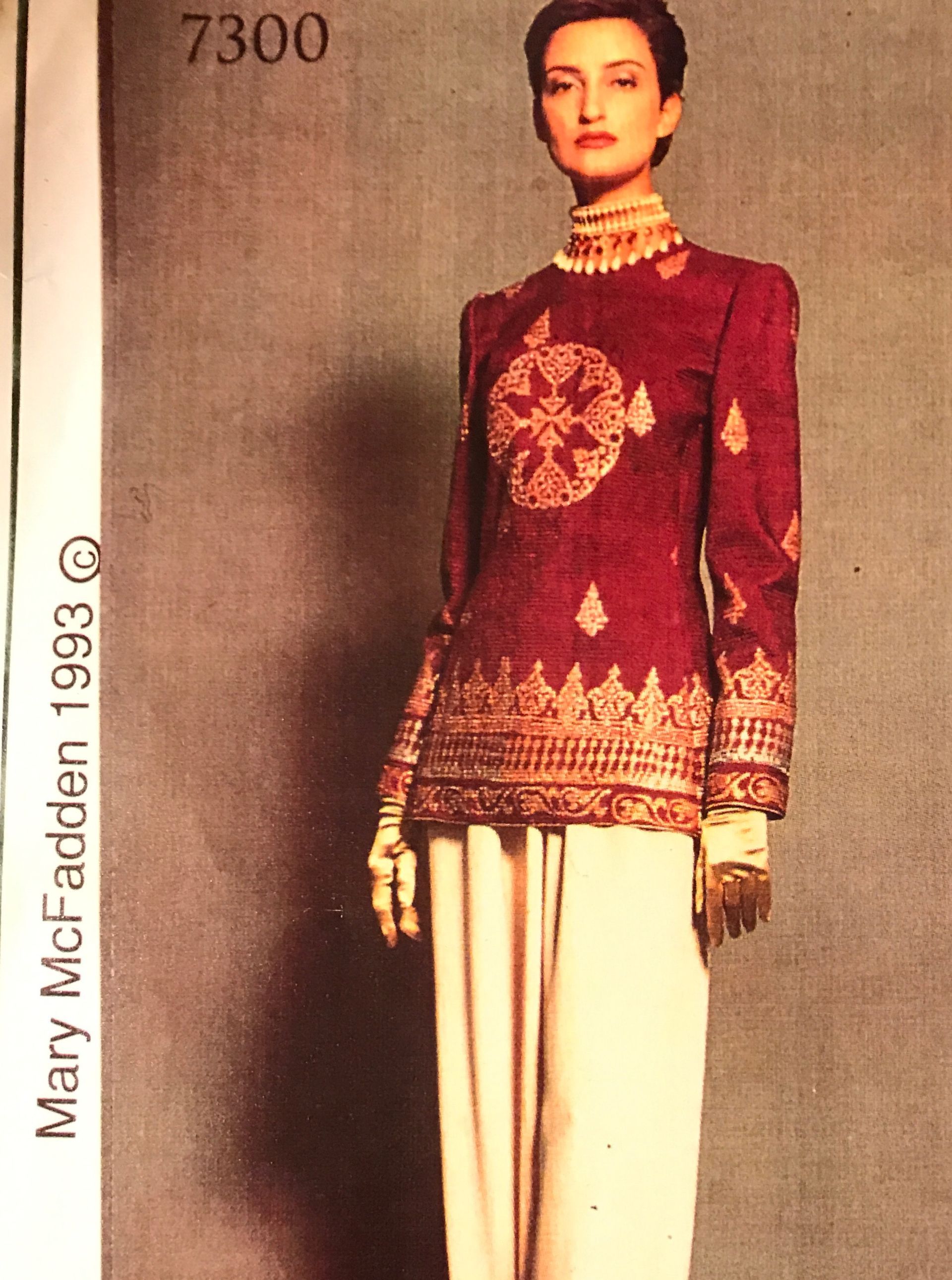 Woman in a burgundy embroidered jacket and white pants.