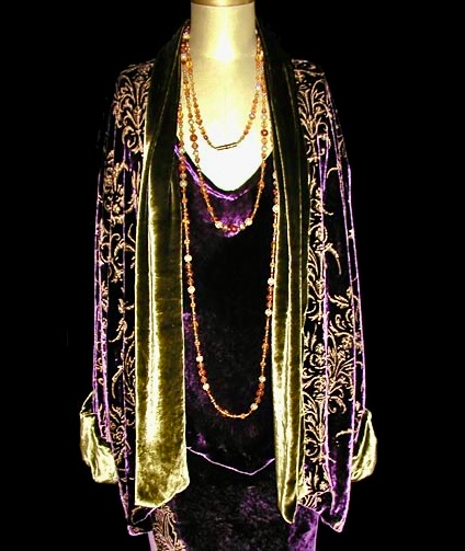 Purple velvet robe over a dark dress with long beaded necklaces; displayed on a mannequin.