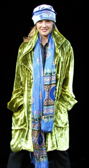 Woman in green velvet coat, blue scarf and patterned head wrap, black background.