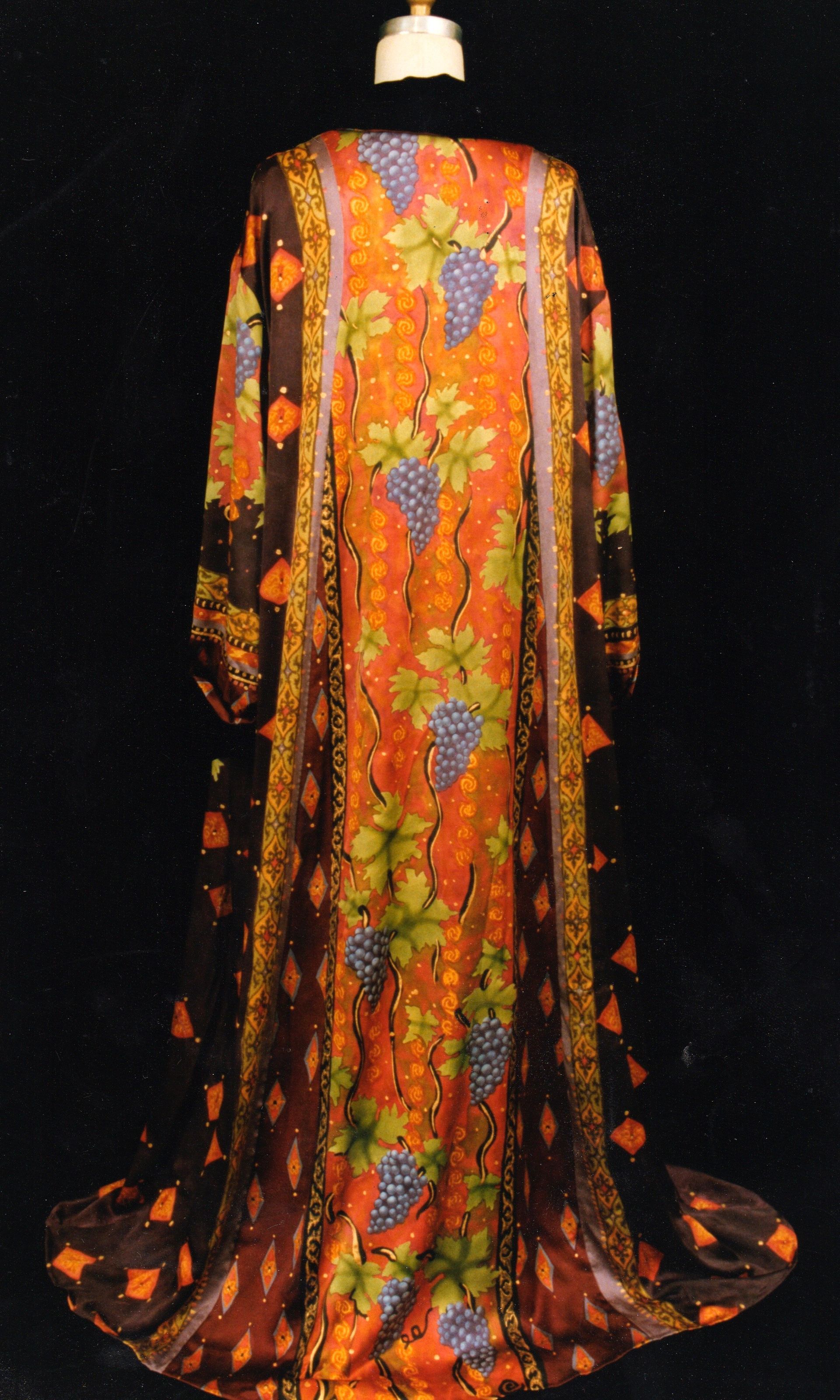 Long, flowing dress with orange and brown floral pattern, including grapes, on a dark background.