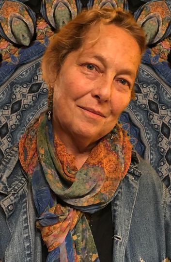 MaryJane wearing a scarf and denim jacket smiling. Background is a patterned blue and gold textile.