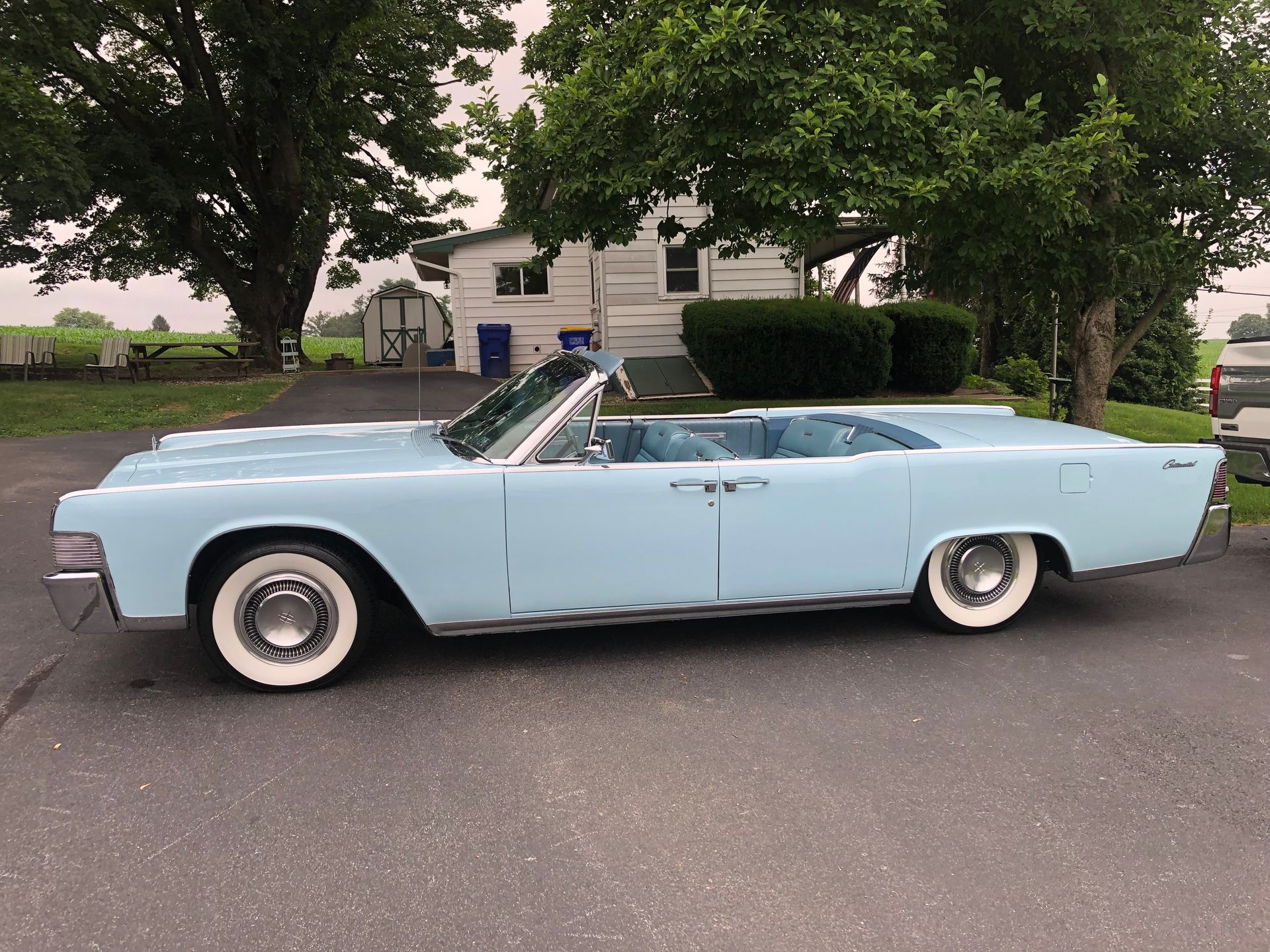 Light blue 1960s Lincoln Continental convertible parked on a driveway in front of a house.