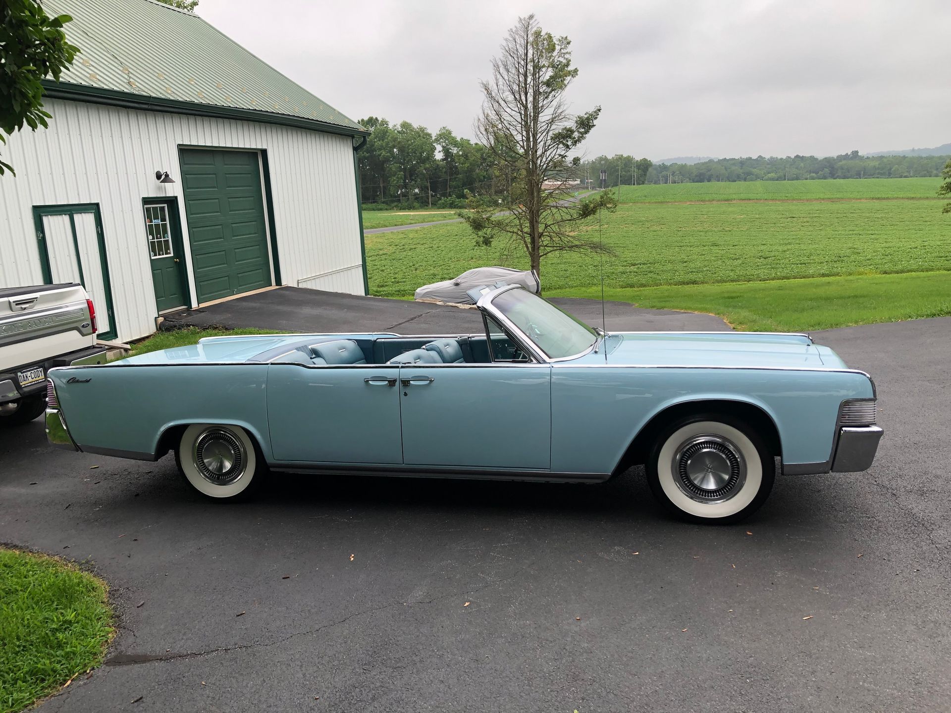 Light blue vintage Lincoln Continental convertible parked in front of a white building with green doors.
