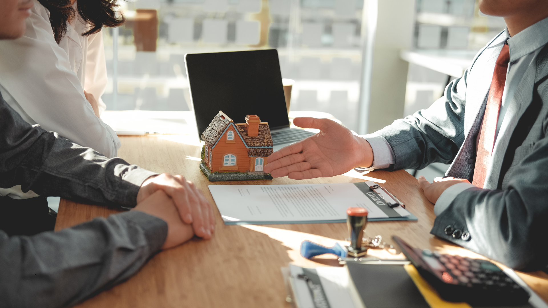 A group of people are sitting at a table with a model house and a laptop.