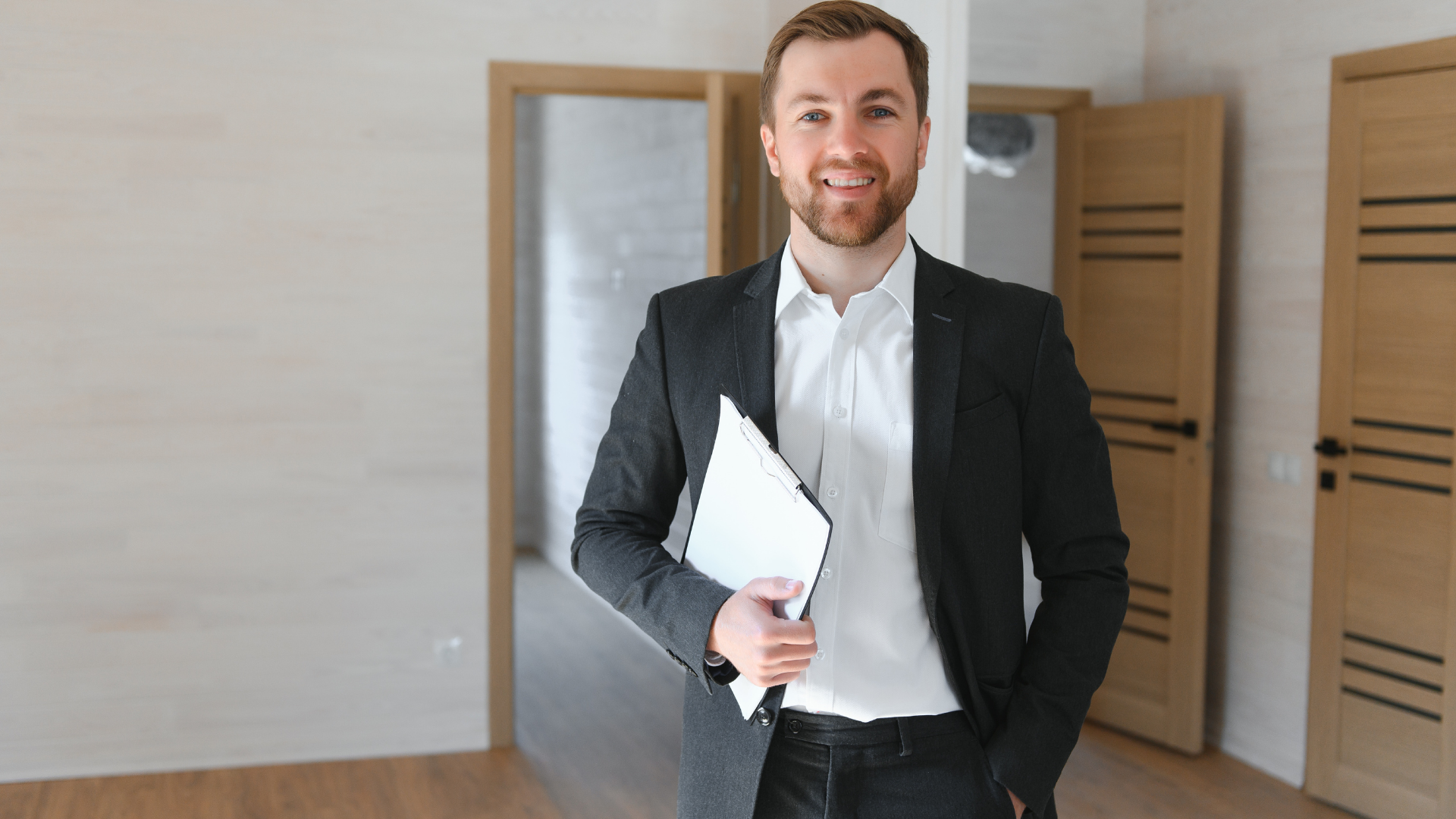 Real estate agent smiles, holding documents, in an empty room with open doors.