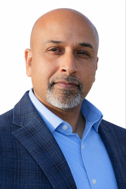 A man in a blue shirt and red tie smiles for the camera