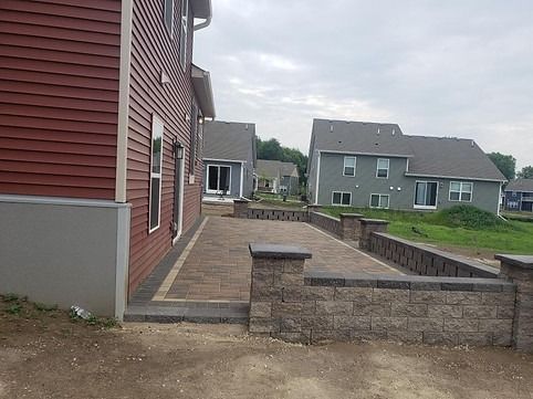 Brick patio and retaining walls adjacent to a red house, with two-story gray houses in the background.