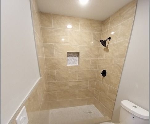 Shower with beige tiles and black fixtures, featuring a recessed shelf and angled walls.