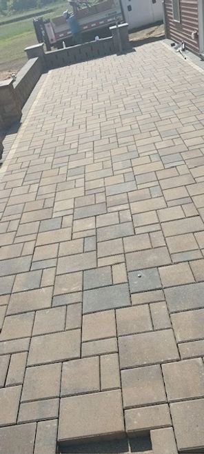 White two-story house with brown roof and gravel driveway. Green lawn with trimmed bushes. Trees in the background.