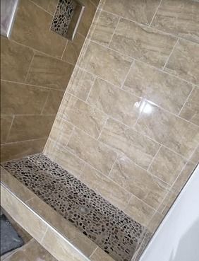 Tiled shower with pebble floor, built-in shelf, and beige walls.