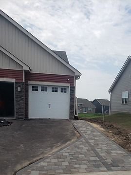 Garage with white door and brick-patterned walkway leading to a new construction residential area.