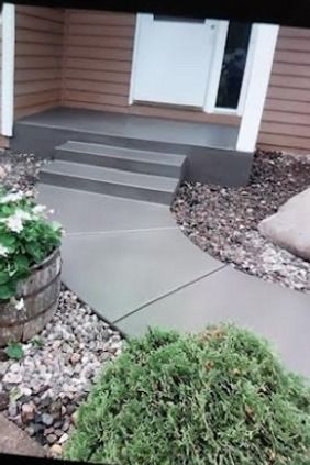 Concrete walkway and steps leading to a front door, with landscaping and a wooden planter.