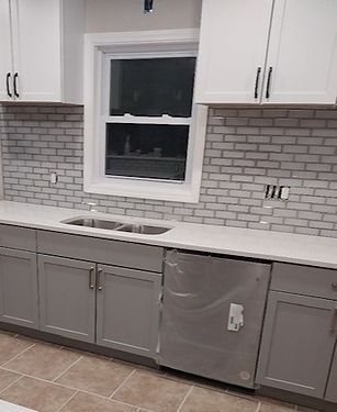 Kitchen with gray and white cabinets, stainless steel dishwasher, white countertop, and white brick backsplash.