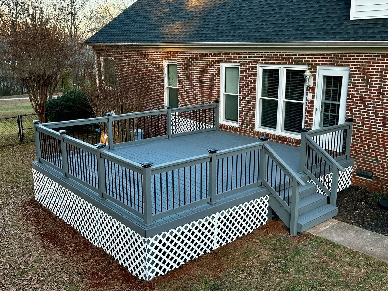Gray wooden deck with lattice skirting attached to a brick house.