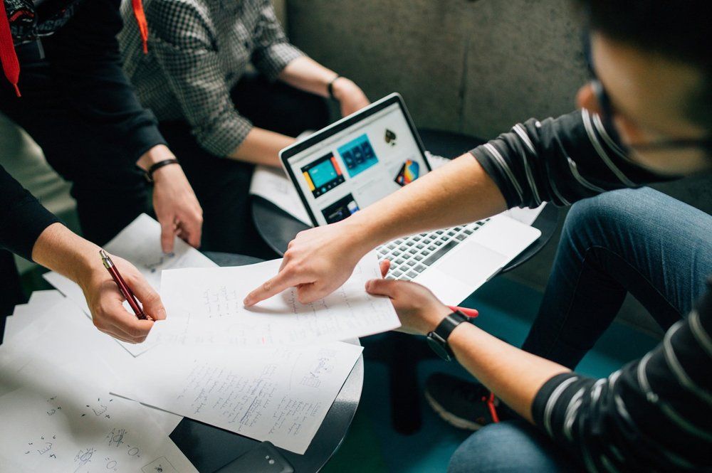A group of people are sitting around a table with papers and a laptop.
