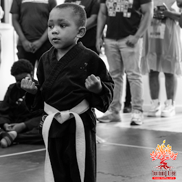Two young boys in karate uniforms are standing next to each other in a dark room.