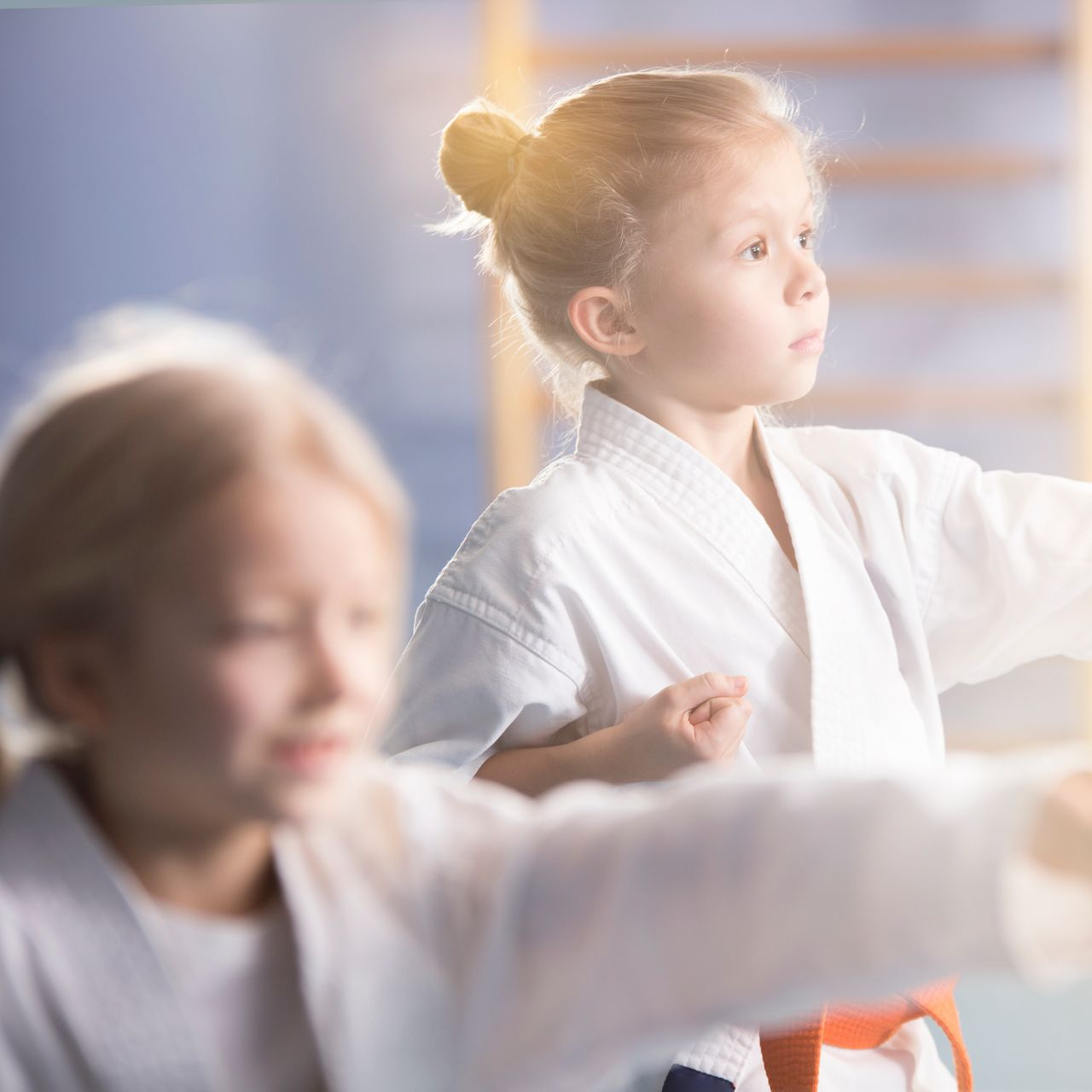 A young girl in a karate uniform is sitting on the floor.