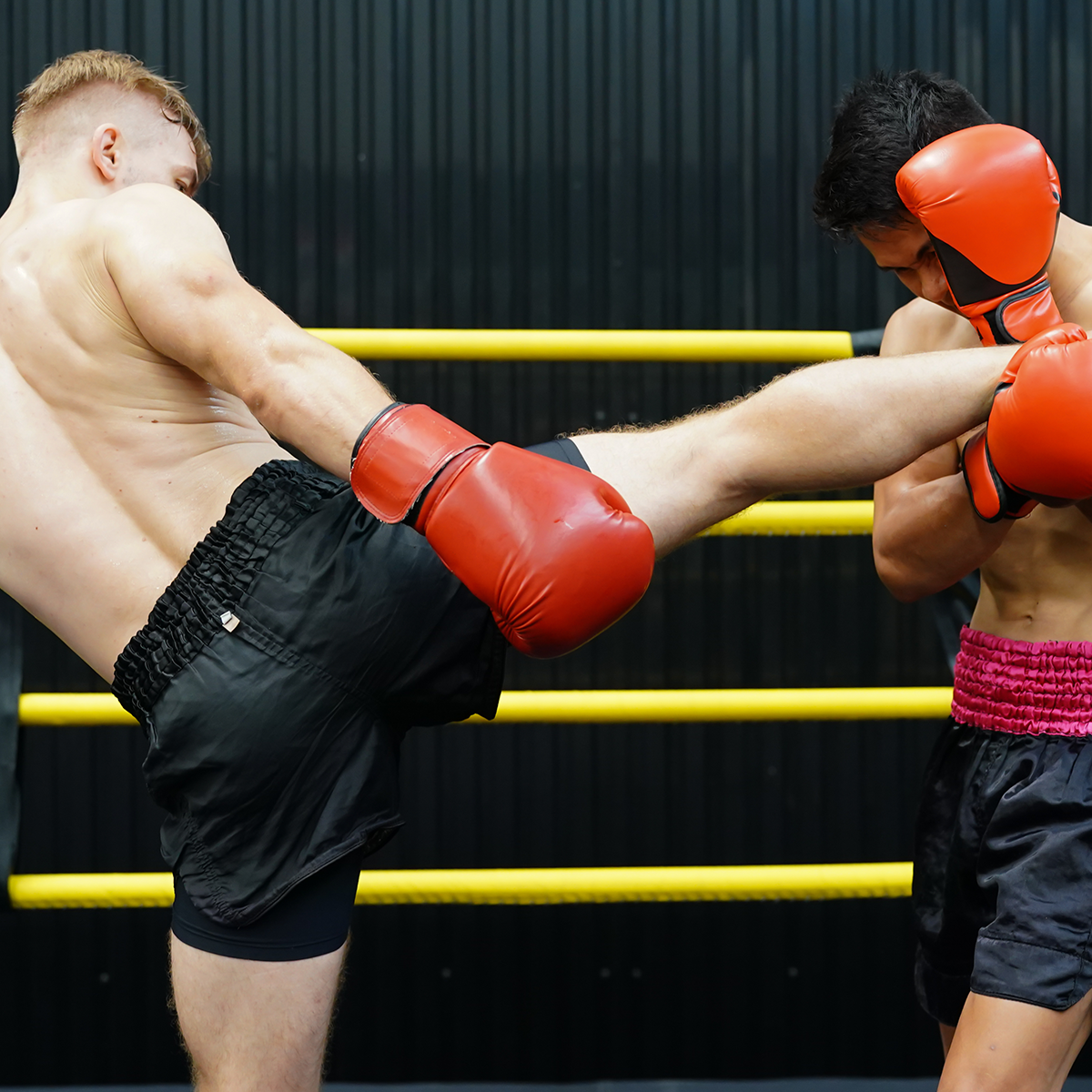 Two men wearing red boxing gloves are fighting in a ring