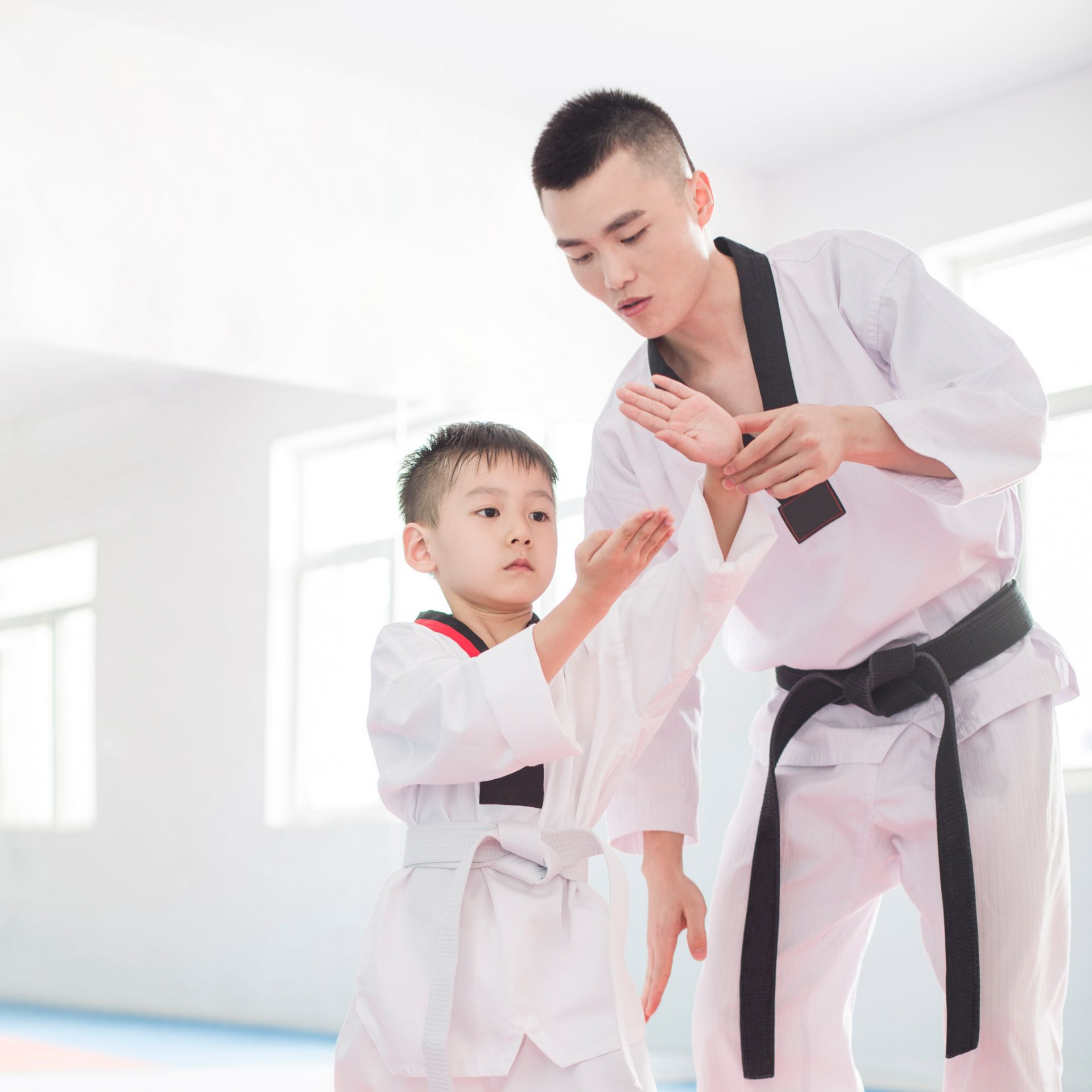 A man is kneeling down next to a young boy in a taekwondo class.