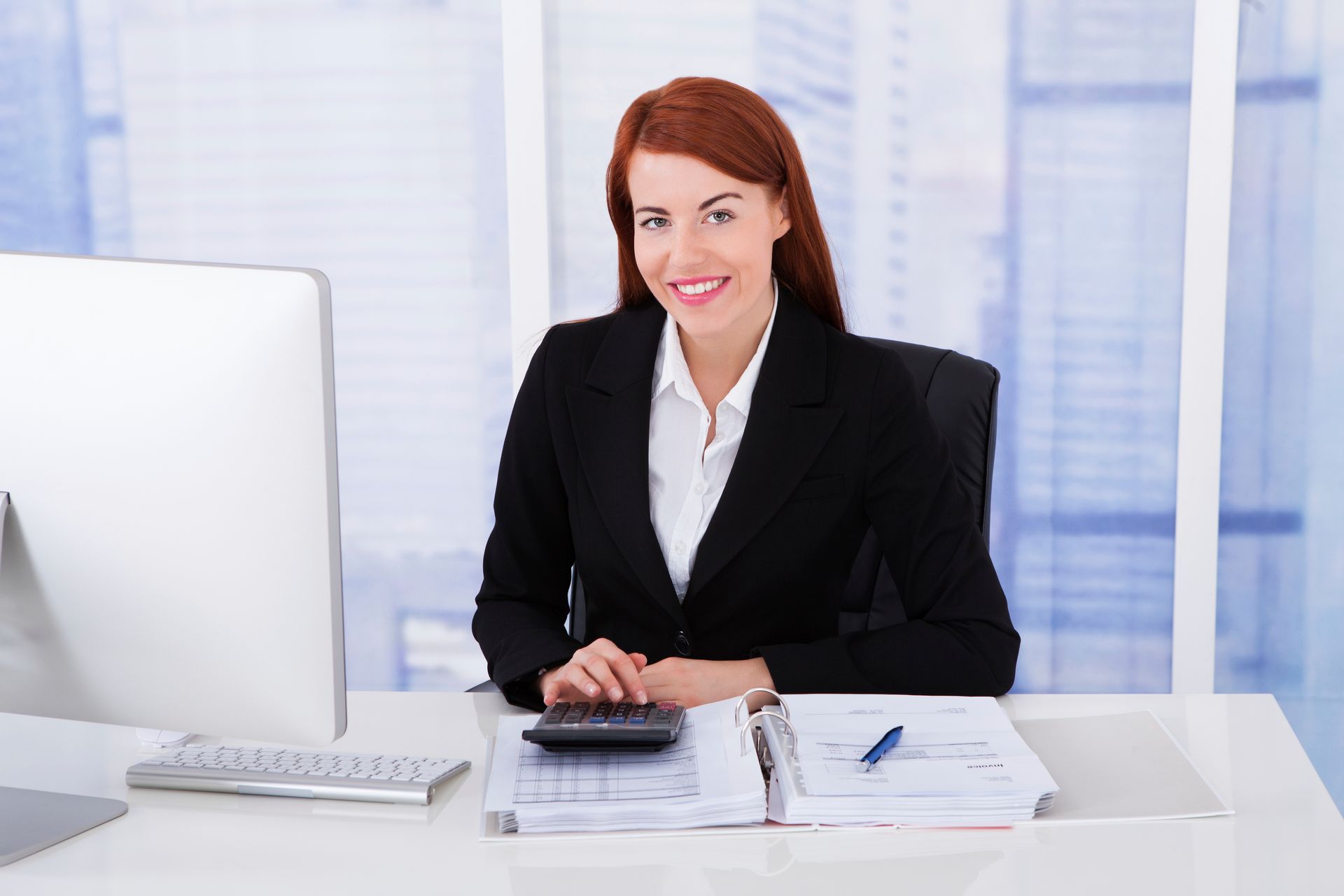 A woman is sitting at a desk with a computer and a calculator.