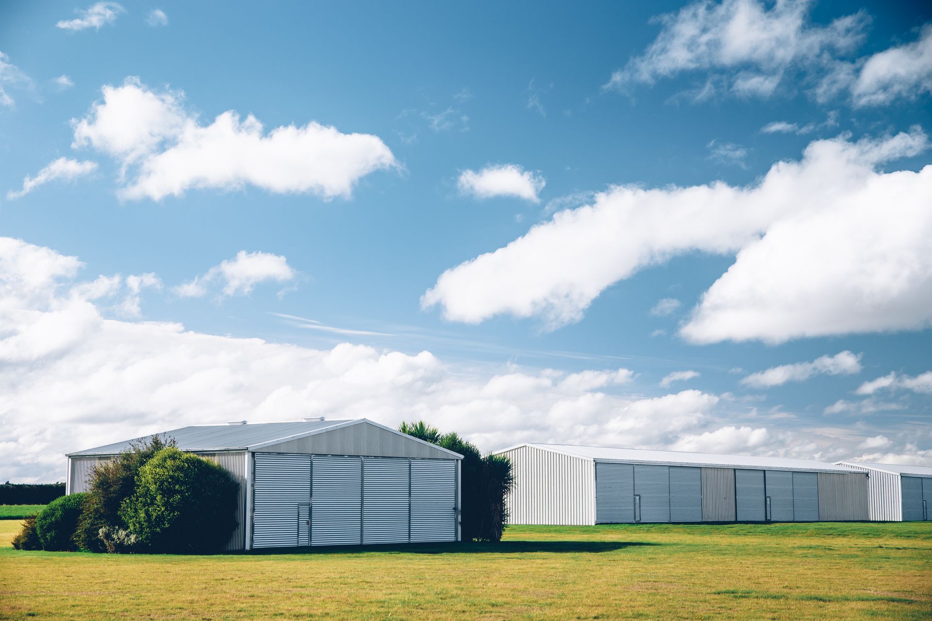 Steel sheds in a row on a green lawn with a cloudy blue sky.