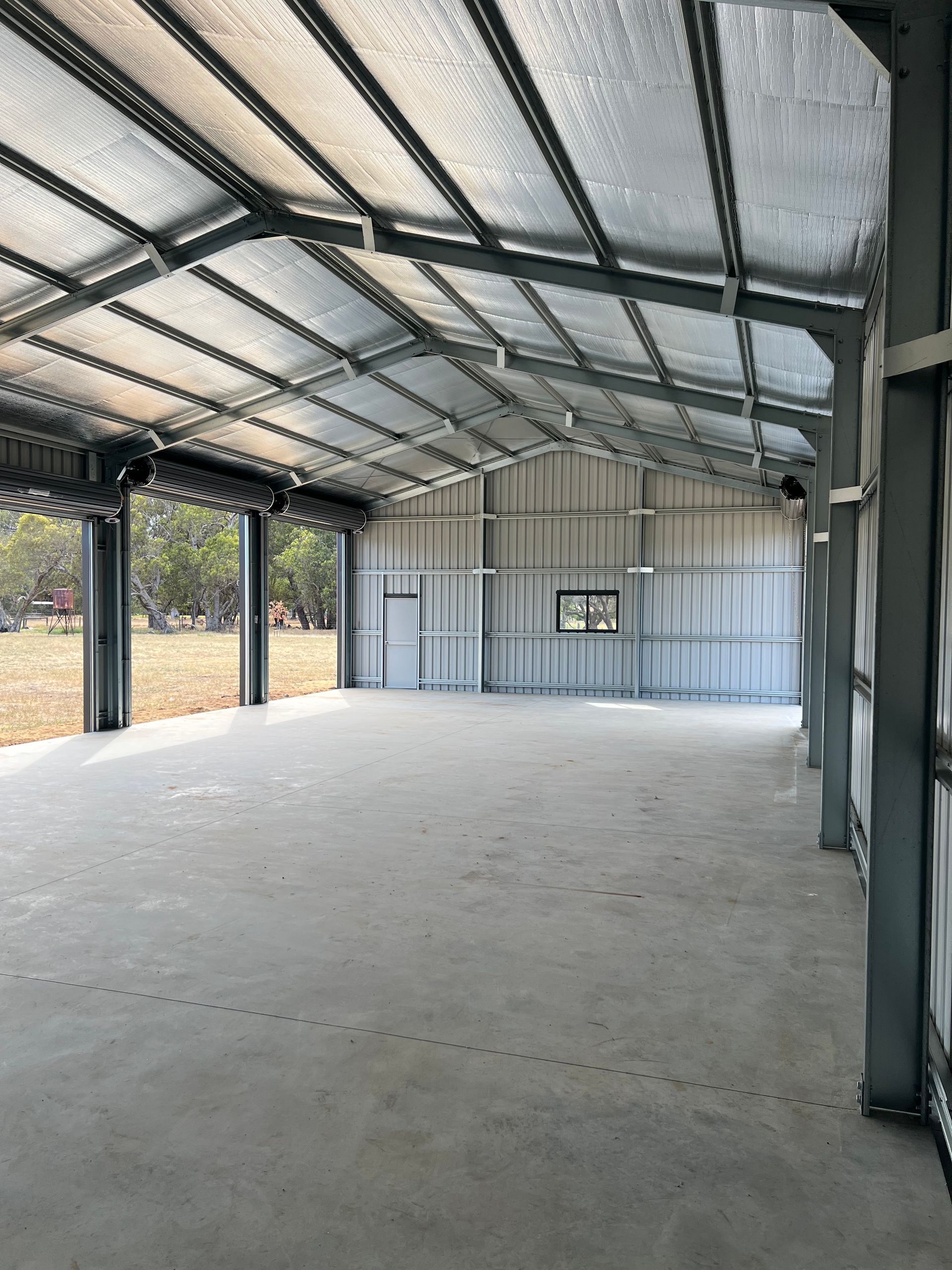 An interior view of a wide-open steel shed with a concrete floor, metal-framed walls, and an insulated roof.