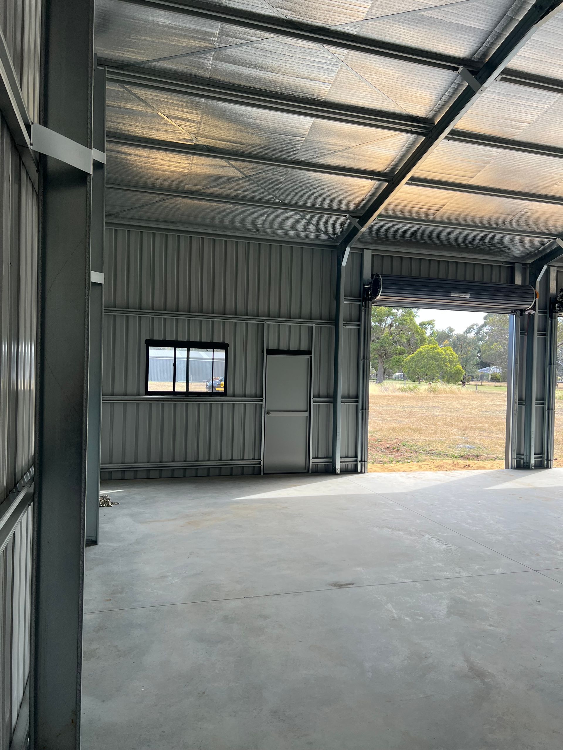 An unfinished metal shed interior with a concrete floor, corrugated walls, and a view through a large open doorway.