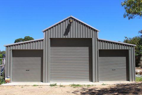 A large metal building with three garage doors and a blue sky in the background.