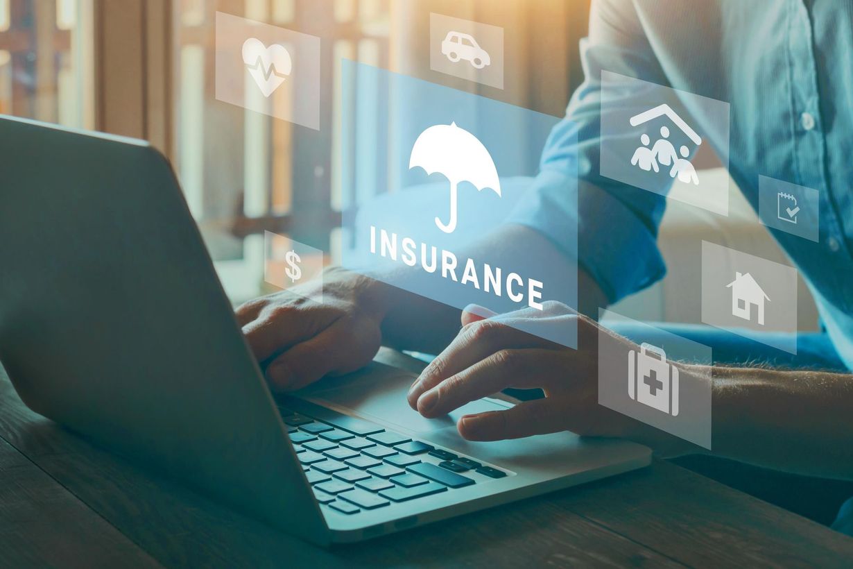 A man is typing on a laptop computer with a screen displaying insurance icons.