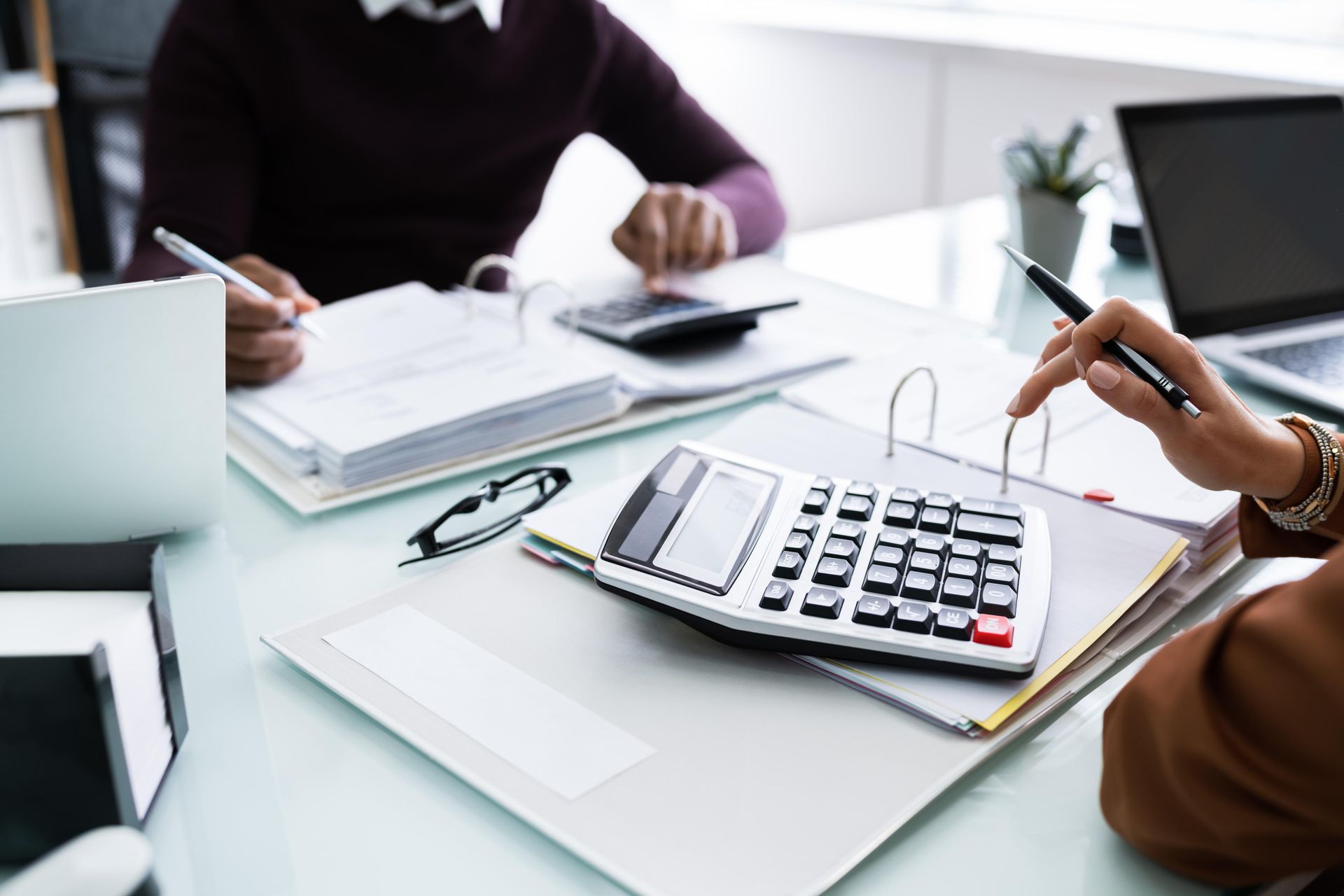 Two people are sitting at a table with a calculator and a laptop.