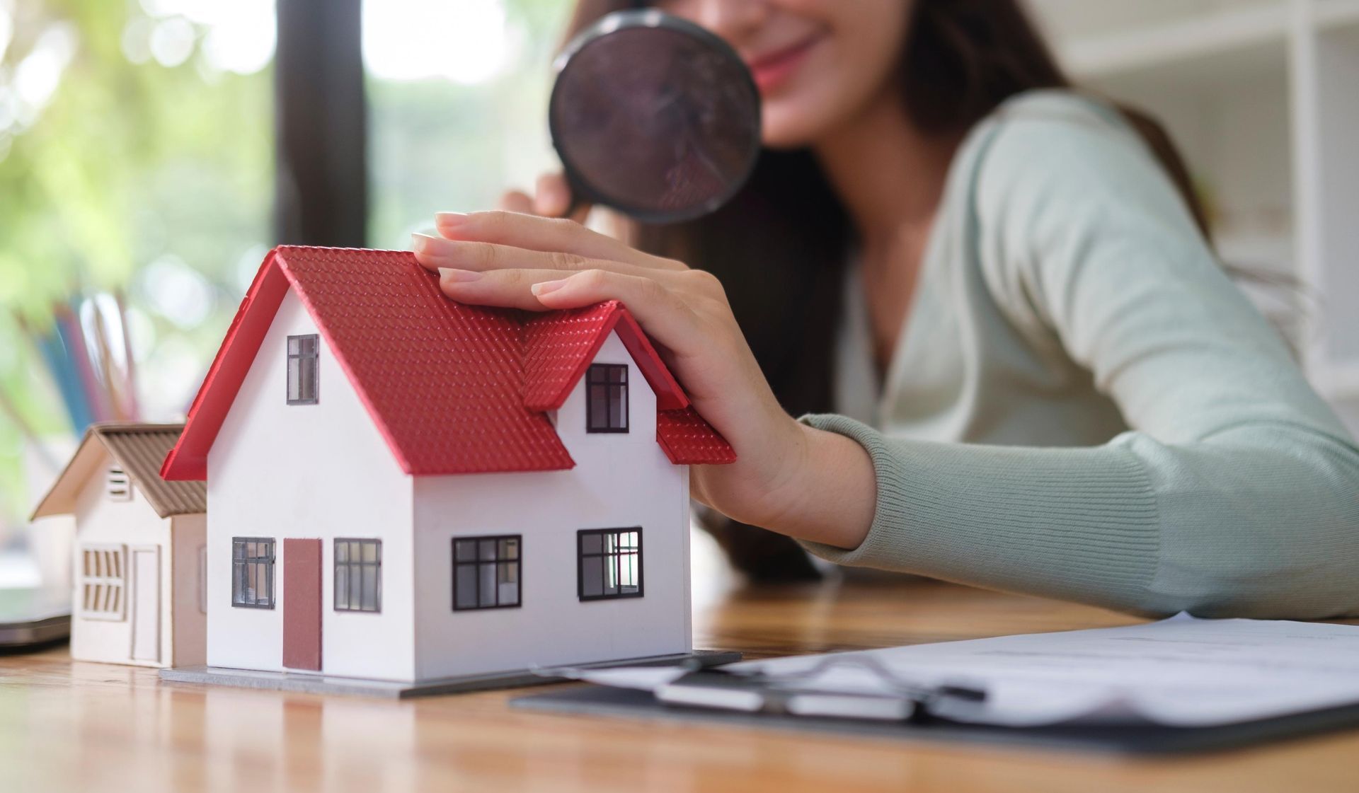 A woman is looking at a model house through a magnifying glass.