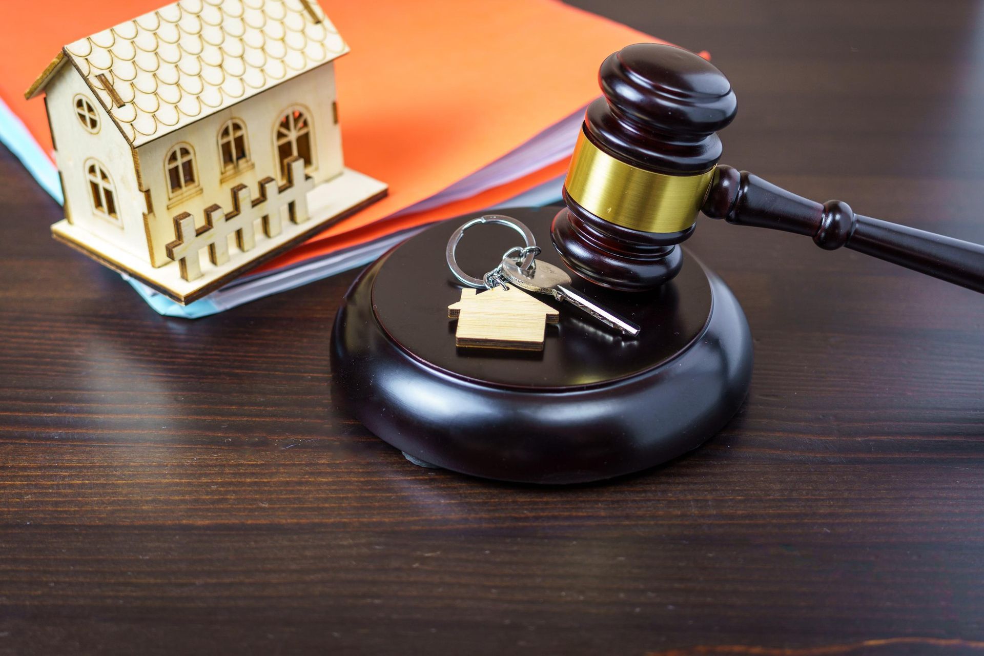 A wooden judge 's gavel is sitting on a wooden table next to a model house and keys.