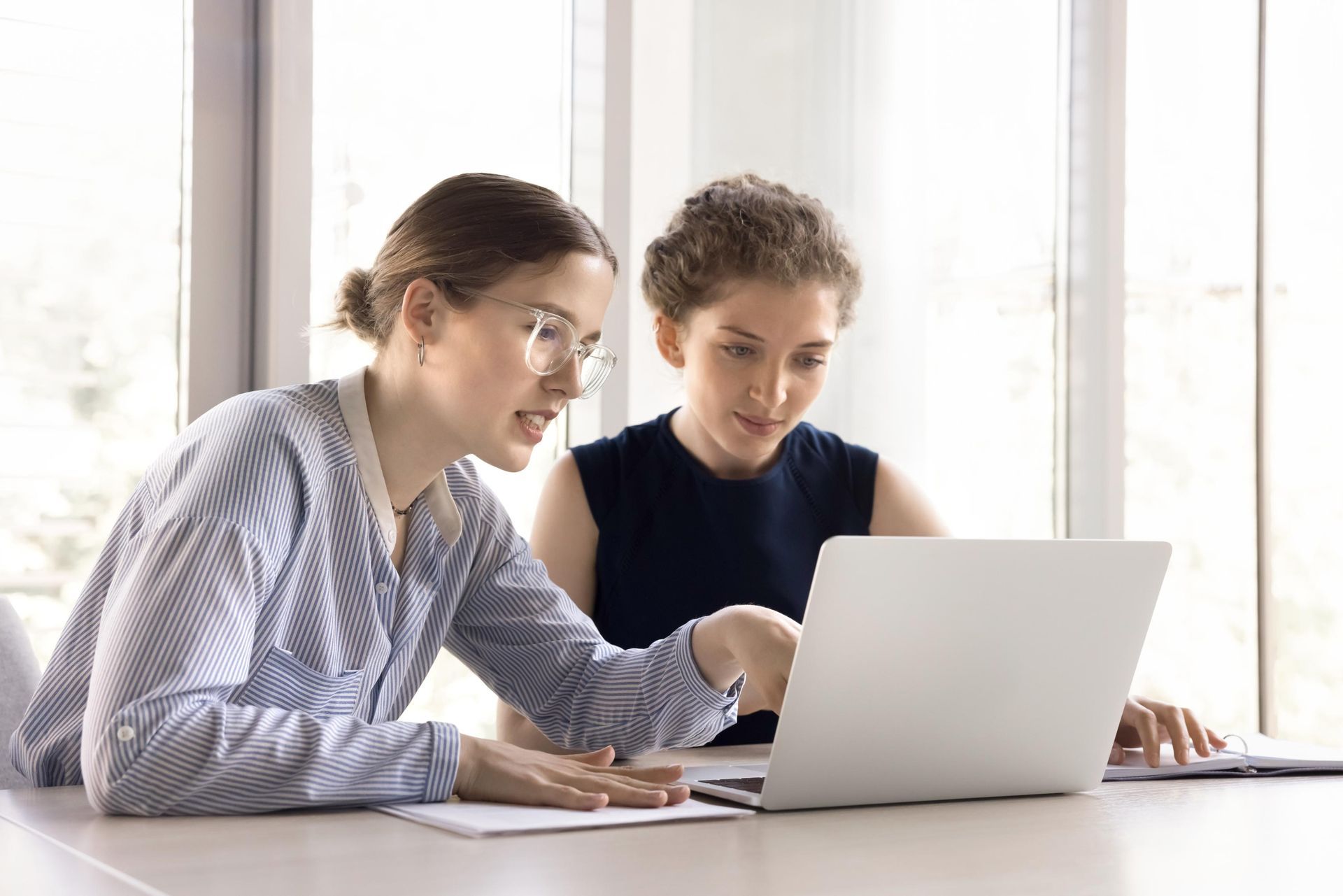 Two women are sitting at a table looking at a laptop computer.